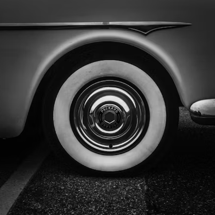 Close-up black and white photograph of a classic car's whitewall tire and chrome hubcap