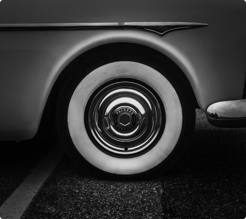 Close-up black and white photograph of a classic car's whitewall tire and chrome hubcap